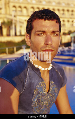 L'homme, jeunes, sérieusement, voir l'appareil photo, portrait, portrait d'homme de la lumière du soir, aux cheveux bruns, dorés, T-shirt, collier, chaîne de moules, des bijoux, des vacances, des loisirs, de l'été, à l'extérieur Banque D'Images