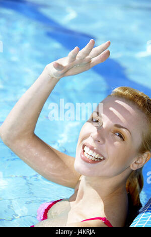 Piscine, femme, jeune, blond, stand, de l'eau, voir l'appareil photo, geste, portrait de 20 à 30 ans, sourit, s'estompe heureusement, sympathique, le soleil, la main, protection, protéger, de l'équilibre, de satisfaction, heureusement, fun, l'amusement, col, rafraîchissements, de refroidissement, de détente, de repos, de profiter, de loisirs, vacances, vacances à la mer, les vacances d'été, la piscine, l'été Banque D'Images