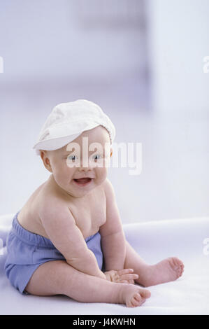 Bébé, s'asseoir, caps, cap, voir l'enfant, petit appareil photo, 5 mois, bébé, couleur des yeux bleu, couleurs vives, rire, les culottes de plastique, à l'intérieur, la conception, le développement, l'enfance, l'innocence, la délicatesse, la gaieté, l'insouciance, de la nature Banque D'Images