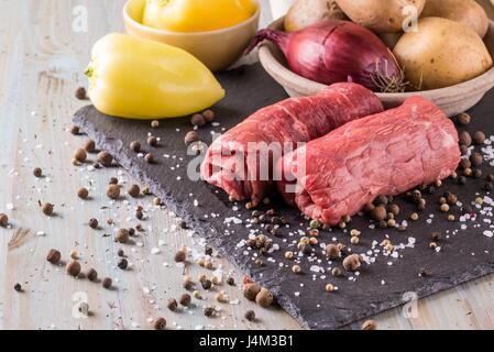 Photo horizontale de deux tranches de boeuf roulé. Roulade de viande est préparé pour et placés sur la pierre d'ardoise noire avec de nombreuses épices et le sel. Légume est à Banque D'Images