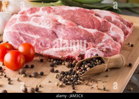 Photo horizontale avec plusieurs coupes de viande de porc de cou. La viande a une teneur en matières grasses sur le côté. Plusieurs épices comme le poivre est renversé autour avec du sel. Légumes Banque D'Images