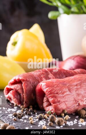 Photo verticale de deux tranches de boeuf roulé. Roulade de viande est préparé pour et placés sur la pierre d'ardoise noire avec de nombreuses épices et le sel. Légume est trop Banque D'Images