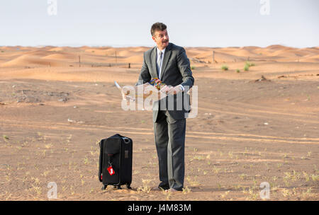 Businessman with a suitcase dans un désert, en regardant une carte d accès Banque D'Images