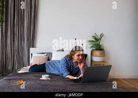 Caucasian woman laying on bed using laptop Banque D'Images