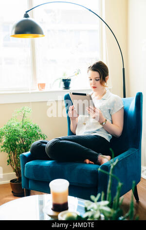 Woman sitting in armchair using digital tablet Banque D'Images