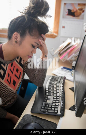 Frustrés Mixed Race woman sitting at desk using computer Banque D'Images