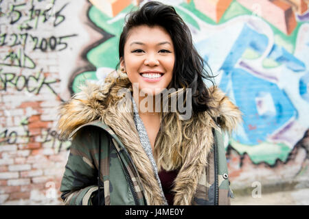 Portrait of smiling Mixed Race woman standing près de l'écriture Graffiti Banque D'Images