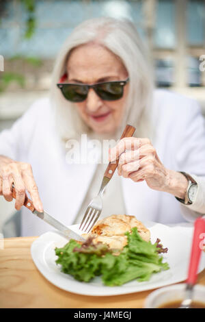 Older Caucasian woman couper les aliments sur la plaque Banque D'Images