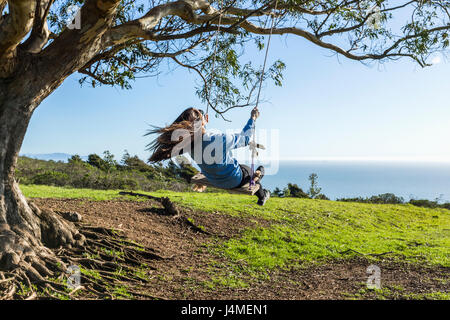 Caucasian woman on tree swing près de ocean Banque D'Images