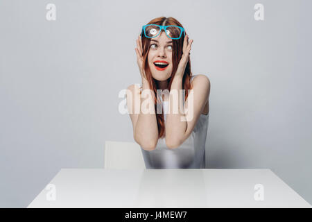 Happy young woman sitting at table lunettes bleu de levage Banque D'Images