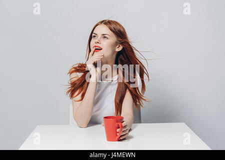 Pensive Caucasian woman sitting at table windy holding red cup Banque D'Images