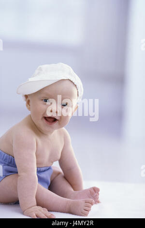 Bébé, s'asseoir, caps, cap, voir l'enfant, petit appareil photo, 5 mois, bébé, couleur des yeux bleu, couleurs vives, rire, les culottes de plastique, à l'intérieur, la conception, le développement, l'enfance, l'innocence, la délicatesse, la gaieté, l'insouciance, de la nature Banque D'Images