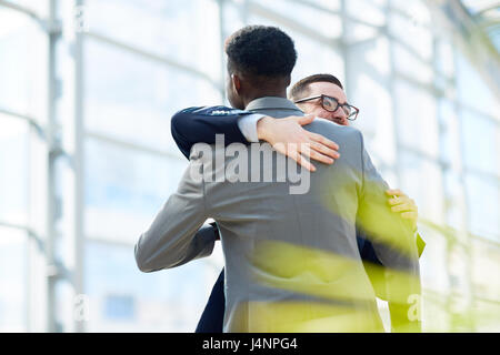Portrait de deux partenaires d'affaires hugging et souriant avec bonheur l'article en verre moderne hall d'immeuble de bureaux Banque D'Images