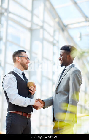 Portrait of smiling businessman greeting Afro-américain par partenaire permanent poignée en verre moderne hall d'immeuble de bureaux Banque D'Images