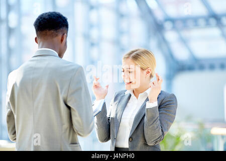 Portrait de deux jeunes business woman talking to African collègue émotionnellement et traverser les doigts dans l'espoir de succès, standing in glass hall de moder Banque D'Images
