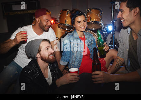 Les jeunes contemporains, trois hommes et une femme, faire la fête dans une boîte de nuit : boire de la bière et s'amusant assis sur scène Banque D'Images
