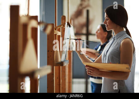 Side view portrait of young female student in art class, profitant de peinture huile Photo sur toile Banque D'Images