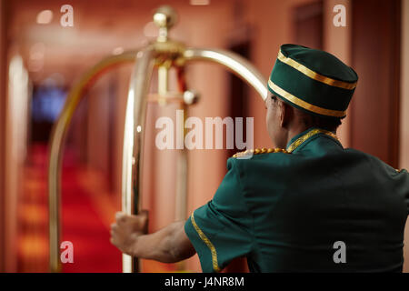 Vue arrière portrait d'Afro-Américain groom poussant chariot à bagages sacs livraison à une chambre d'hôtel dans un couloir, d'aider les clients Banque D'Images