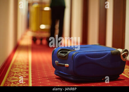 Photo de gros plan transport des bagages groom dans couloir de l'hôtel, l'accent sur valise bleue sur marbre par la porte de la chambre Banque D'Images