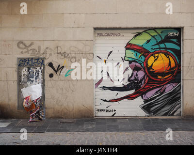 Un Ieza Nebbia street art graffiti d'un casque le casque sur la tête porte de garage dans le mur de bloc avec les déchets papier corbeille blowing in wind Valencia Espagne Banque D'Images