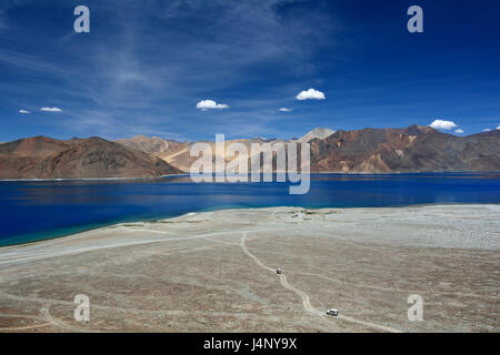 Vue panoramique sur le lac Pangong : au premier plan il y a un énorme tas de sable clair, la route à travers les voitures passer, l'eau bleu foncé du lac, le Banque D'Images