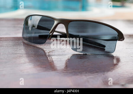 Lunettes de soleil sur la table en bois brun proche piscine Banque D'Images