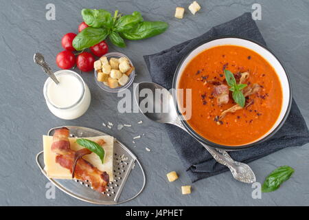 Soupe de tomates au basilic épais et lard grillé dans un bol en céramique noire sur un fond gris. Concept de saine alimentation. Banque D'Images