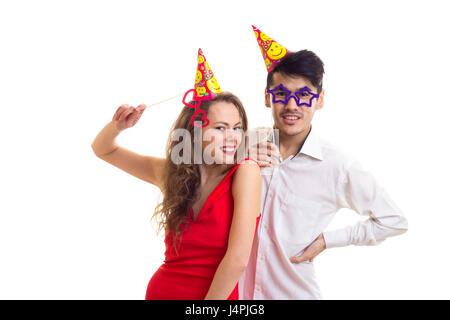 Jeune femme séduisante avec de longs cheveux châtains en robe rouge et les jeunes bel homme en chemise blanche avec la célébration de chapeaux en tenant la carte bâtonnets de verres Banque D'Images