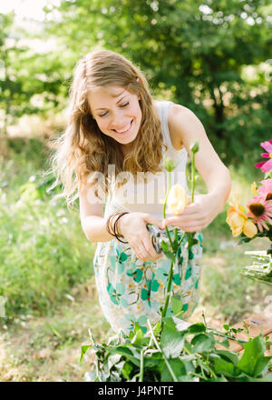 Bouquet, arrangement floral et concept - smiling young beautiful girl en jardin d'été feuilles coupées de roses jaunes, une main tenant un émondeur, yeux clos, prépare une fleur pour un bouquet Banque D'Images