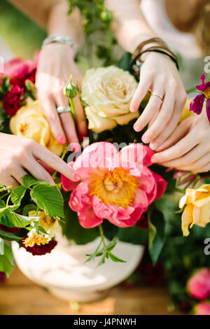 Bouquet, arrangement floral et concept - gros plan sur les mains douces de deux jeunes femmes bouquet élégant de décoration d'été jaune et blanc, roses, pivoines, œillets roses et marguerites Banque D'Images