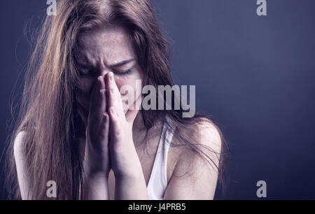 Jeune femme visage pleurant dans ses mains sur un fond sombre Banque D'Images