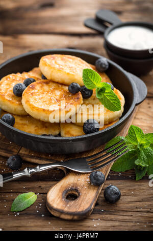 De délicieuses crêpes de fromage cottage ou de bleuets frais avec syrniki en fonte casserole sur fond rustique en bois sombre. Délicieux petit-déjeuner. Banque D'Images