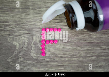 Forme de pilules roses formant F alphabet sur fond de bois Banque D'Images