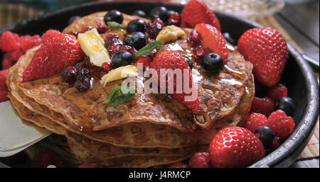 Verser le miel sur un petit déjeuner de crêpes aux fruits rouges et fruits secs Banque D'Images