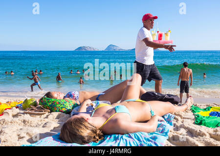 RIO DE JANEIRO - le 5 février 2017 : Un vendeur de plage cocktails caipirinha vente transmet une plage en bikini allongée sur la rive de la plage d'Ipanema. Banque D'Images