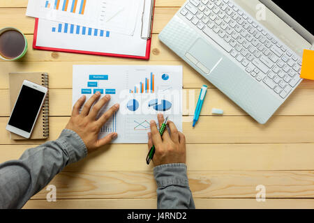 Vue supérieure de la personne d'affaires de discuter de graphiques avec ordinateur portable,café,smartphone,stylo portable sur bureau. Banque D'Images