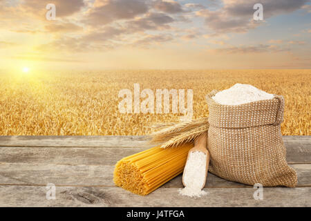 Tas de spaghetti de blé dur, farine de grains entiers dans le sac et scoop sur table avec champ de céréales mûrs sur l'arrière-plan. Photo avec place pour le texte. G Banque D'Images