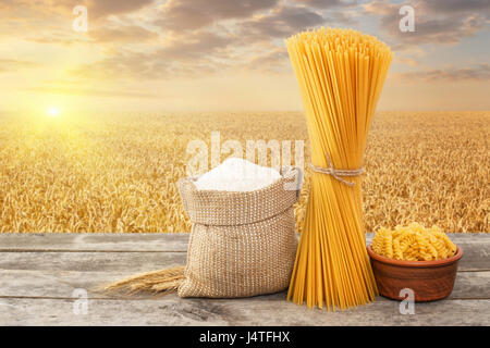 Pâtes crues, en forme de spirale et spaghetti, de farine de farine dans le sac sur table avec champ de céréales mûrs sur l'arrière-plan. Photo avec place pour le texte. Golden w Banque D'Images