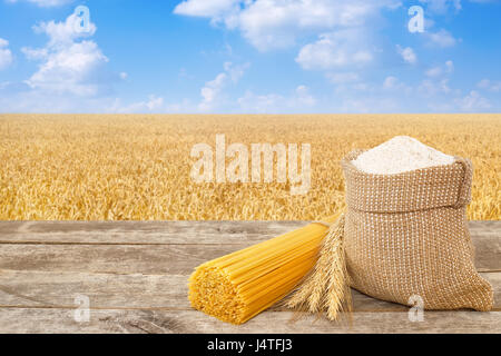 Spaghettis non cuits à partir de blé dur, farine de grains entiers en sac sur table avec champ de céréales mûrs sur l'arrière-plan. Champ de blé doré avec ciel bleu. Guérir Banque D'Images