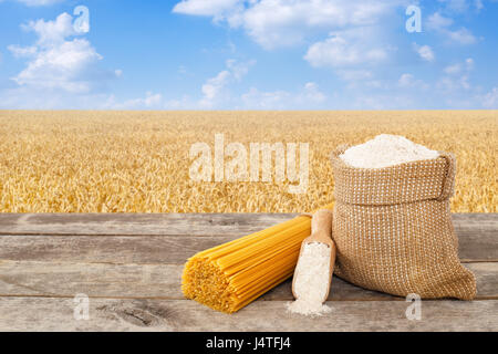 Spaghettis non cuits à partir de blé dur, farine de grains entiers dans le sac et scoop sur table avec champ de céréales mûrs sur l'arrière-plan. Champ de blé doré avec blue Banque D'Images