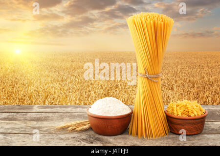 Pâtes alimentaires non cuites à partir de blé dur, farine complète dans un bol sur la table avec champ de céréales sur l'arrière-plan. Champ de blé doré sur le coucher du soleil. Photo avec p Banque D'Images