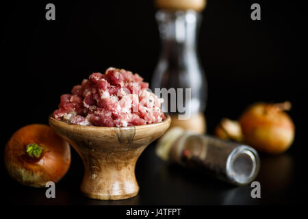 La viande hachée dans un bol en bois avec des épices sur un fond noir Banque D'Images
