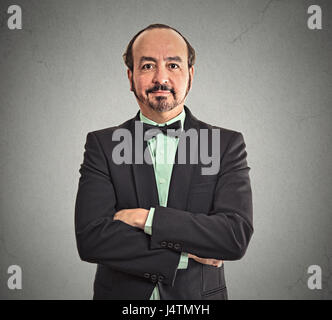 Portrait of smiling profil confiant d'âge moyen à maturité balding businessman wearing costume et noeud papillon avec les bras croisés isolé sur mur gris office b Banque D'Images