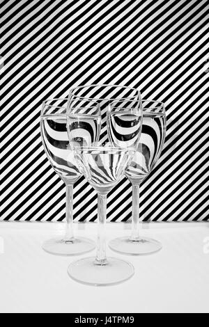 Une sélection de trois verres à vin holding différents niveaux de l'eau, placé devant un arrière-plan noir et blanc à rayures. Banque D'Images