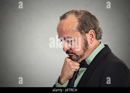 Portrait vue côté homme d'affaires d'âge moyen perplexe pense décider de quelque chose, le menton sur le poing à la sombre mur gris isolé Banque D'Images