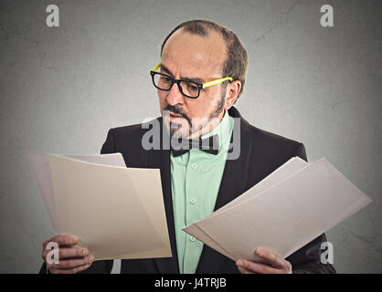 Homme confus avec des lunettes à la tenue des documents à un trop grand nombre de documents contrats isolé sur fond gris mur de bureau. Visage humain expressio Banque D'Images