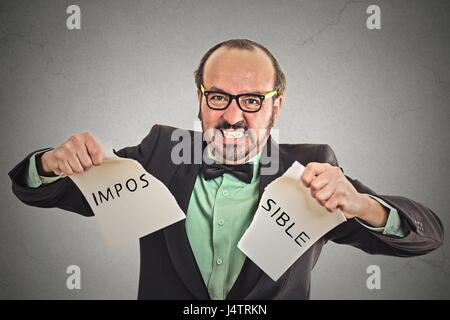 Business man portrait déchirant mot impossible écrit sur papier isolé sur fond de bureau mur gris. Visage humain à la détermination de l'expression de l'émotion Banque D'Images