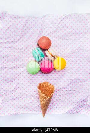Gâteau macarons macarons multicolores ou dans la forme triangle et cornet gaufré sur le blanc avec des pois rose fond. Vue d'en haut. Espace libre pour le texte Banque D'Images