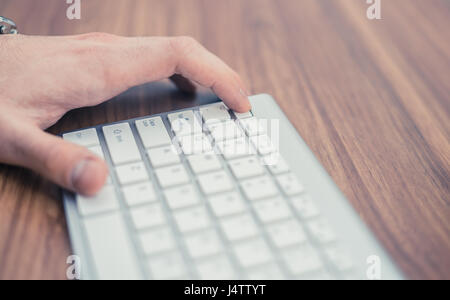 La main de l'homme en appuyant sur le bouton Échap sur Wireless keyboard sur table en bois Banque D'Images