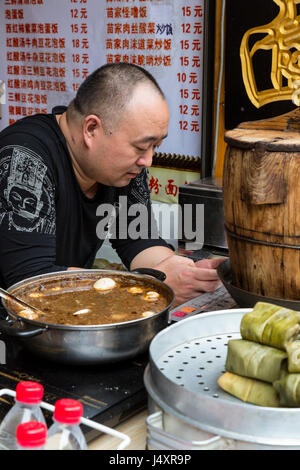 Zhenyuan, Guizhou, en Chine. Magasin de vente d'aliments de collation, l'Homme contrôle son téléphone cellulaire. Banque D'Images